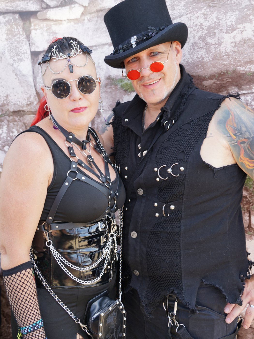 Alexandra und Gerrit Oertgen in schwarzer Festival-Kleidung mit runden Sonnenbrillen vor einer Steinmauer